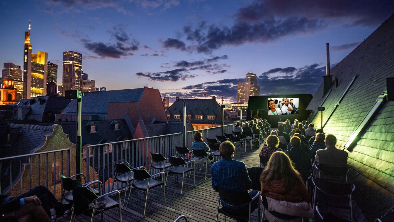 Open-Air Kino auf einer Dachterrasse mit Blick auf die erleuchtete Stadt.