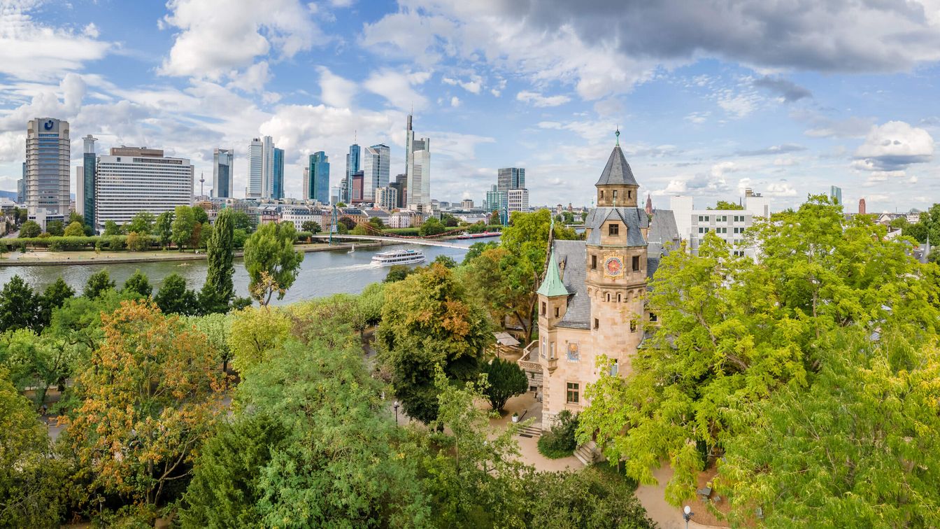 Typical view of Frankfurt, in front the old Villa Liebieg between trees, a ship sails on the Main, skyscrapers in the back.