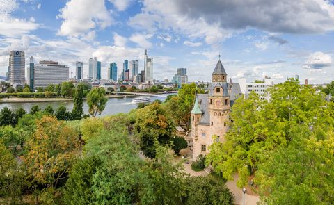 Blick über Bäume auf Museumsufer und Skyline mit Main in Frankfurt.