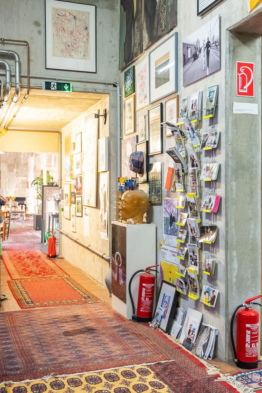 Kreatives Atelier mit bunten Teppichen, Bildern, orange Sofa, Fahrrad und Kunst.