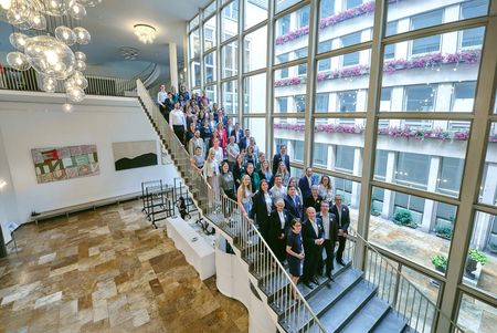 Group photo on staircase in bright hall with large window fronts.