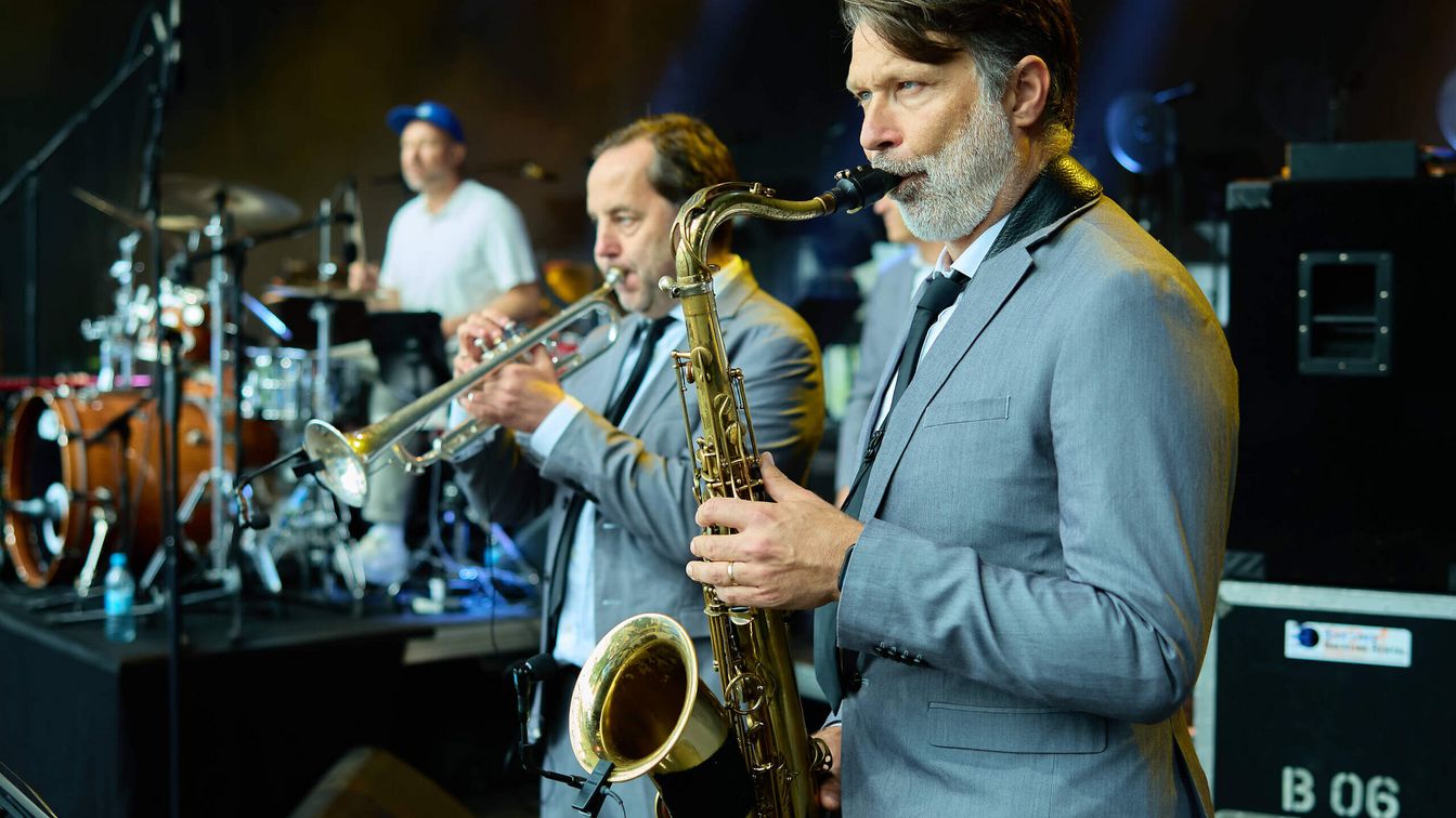 Zwei Musiker spielen Trompete und Saxophon auf einer Bühne. 