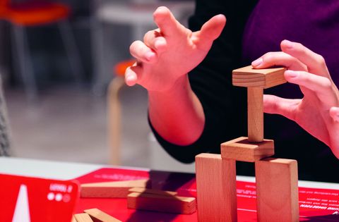 Hände stapeln Holzklötze auf rotem Tisch bei einem kreativen Workshop.