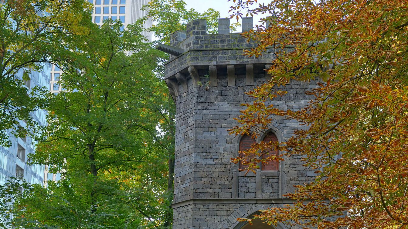 Ein Zierturm im Rothschildpark eingebettet in Herbstlaub, im Hintergrund moderne Hochhäuser